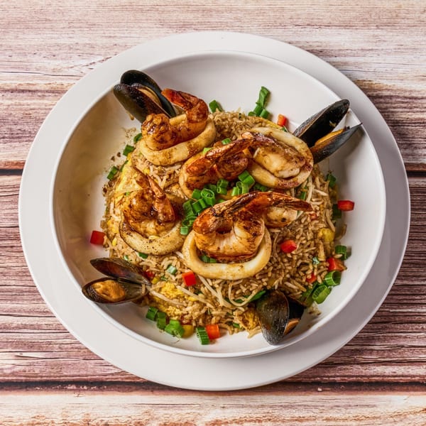 Peruvian chaufa de mariscos with shrimp, squid, and mussels on fried rice in a white bowl.