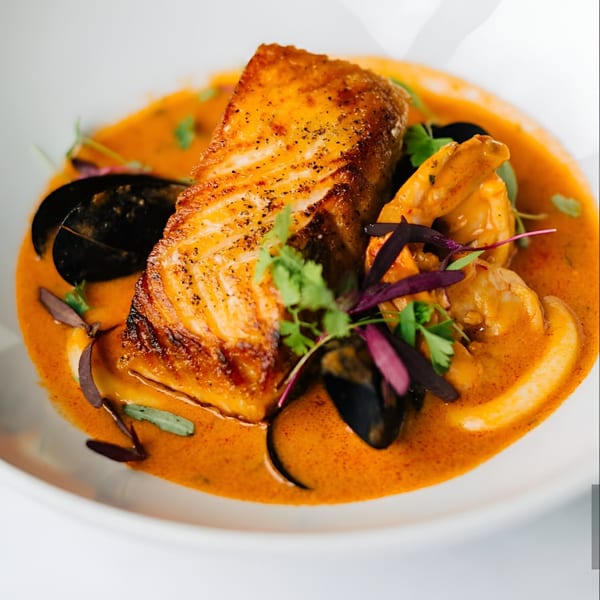 Peruvian seafood dish with seared salmon, mussels, shrimp, and calamari in a vibrant orange sauce.
