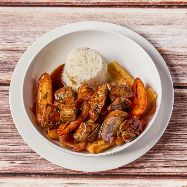 Peruvian Lomo Saltado with beef, vegetables, rice, and fried yuca in a white bowl.