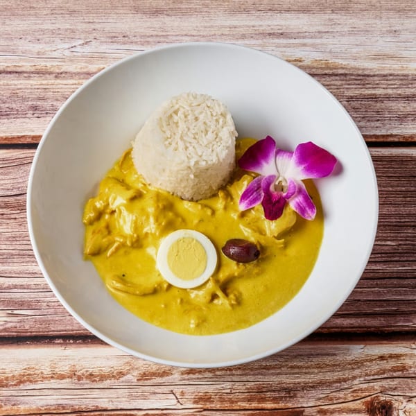 Peruvian Aji de Gallina with rice, a hard-boiled egg, olive, and purple orchid in a white bowl.